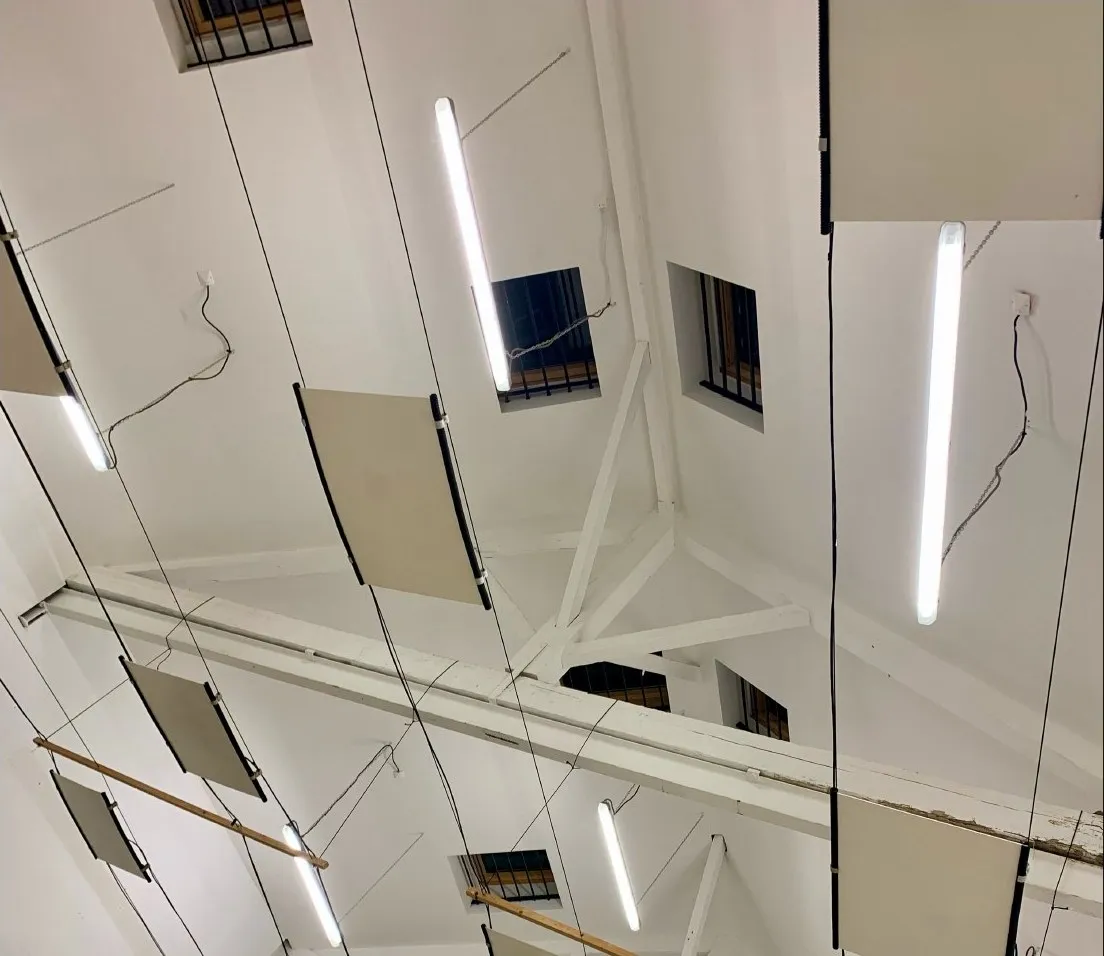 Vue plongeante d'une installation suspendue — panneaux et néons sous la charpente blanche
