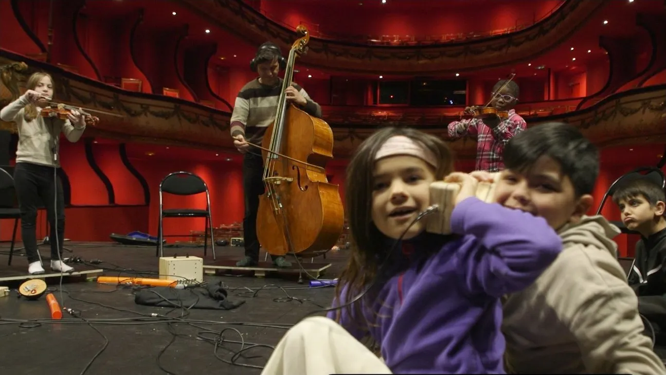 Atelier Écouter Autrement au Théâtre du Jeu de Paume — enfants tenant un boîtier vibrant pendant qu'une contrebassiste joue en arrière-plan