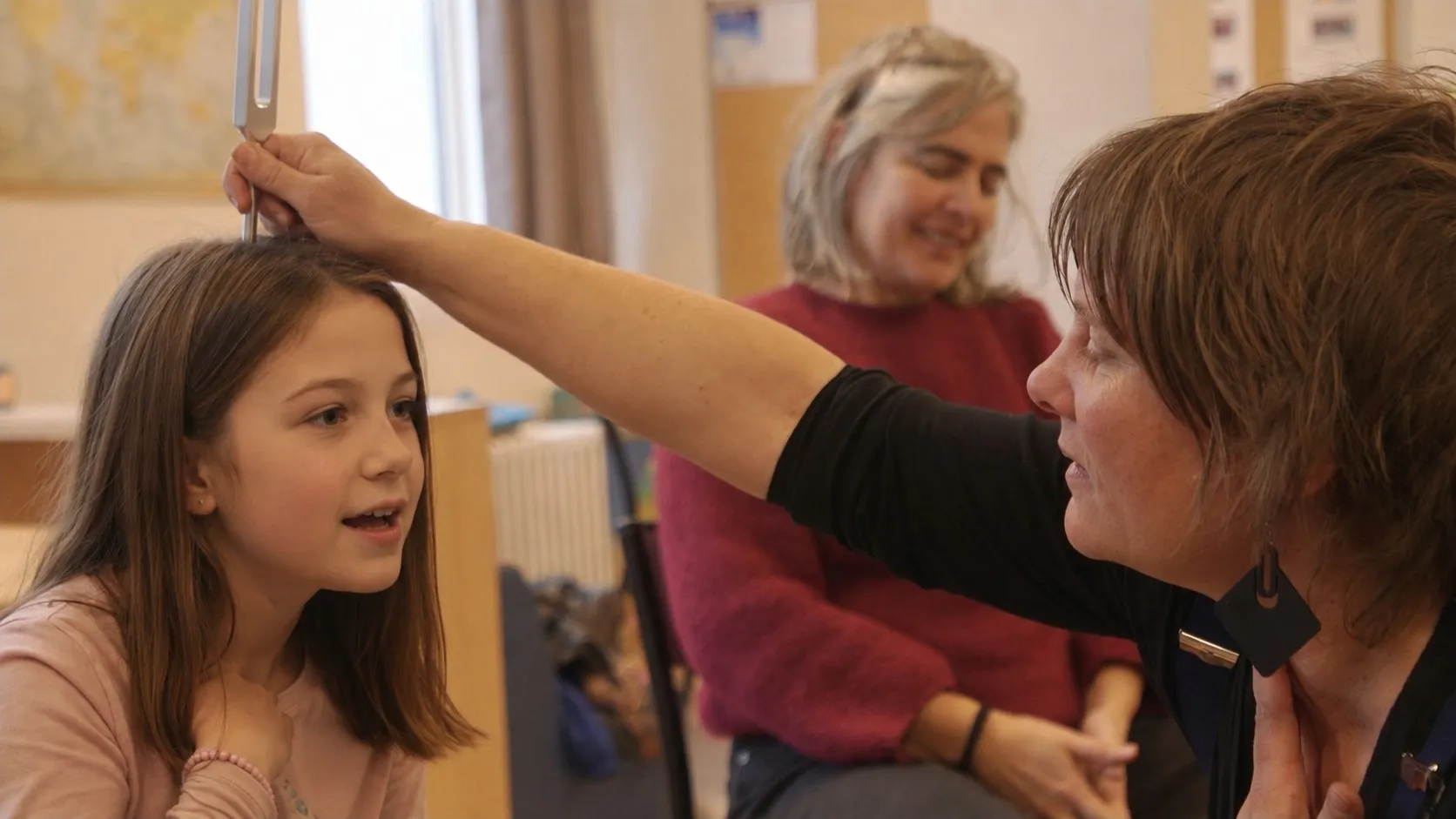 Médiatrice posant un diapason sur le crâne d'une fillette en atelier — exploration tactile du son