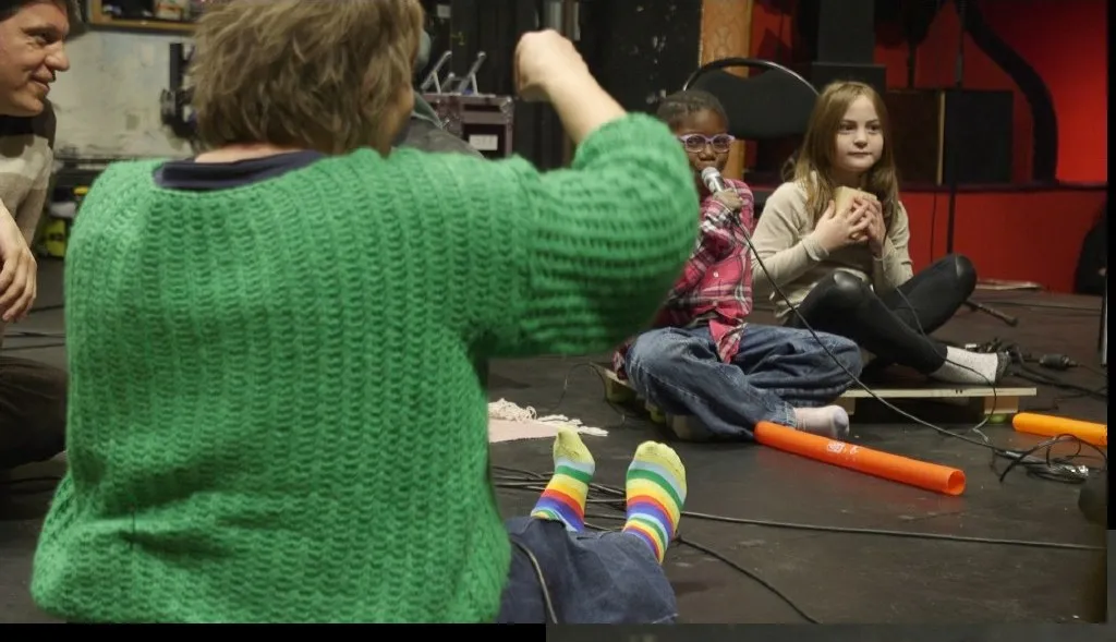 Atelier collectif sur scène — un médiateur accompagne plusieurs enfants à l'écoute tactile